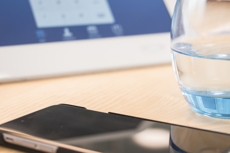 Imagen de una mesa con un vaso de agua, una tablet y un teléfono móvil. 