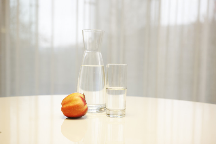 Imagen de una mesa con una jarra de agua, un vaso con agua y una manzana. 